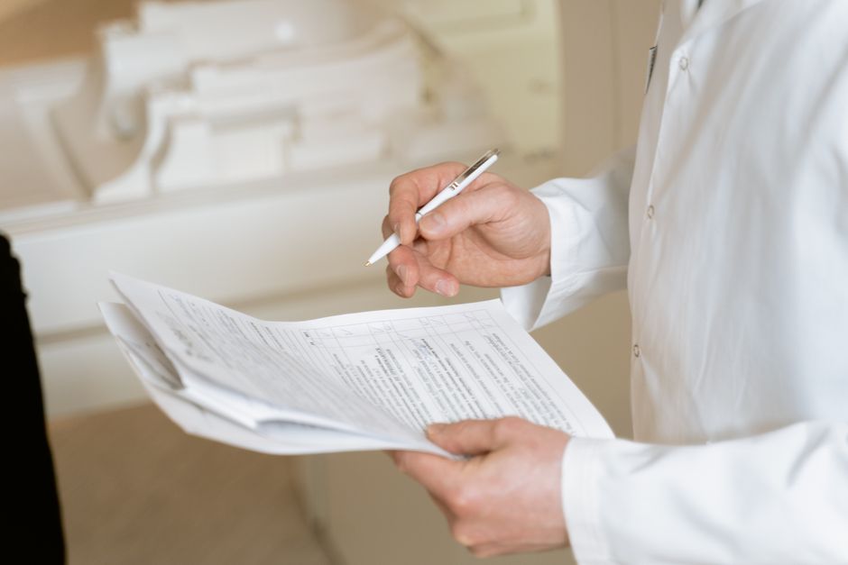 A person dressed in a white shirt is holding and reviewing a detailed house removals checklist printed on multiple sheets of paper, using a pen to point at specific items. The background shows part of